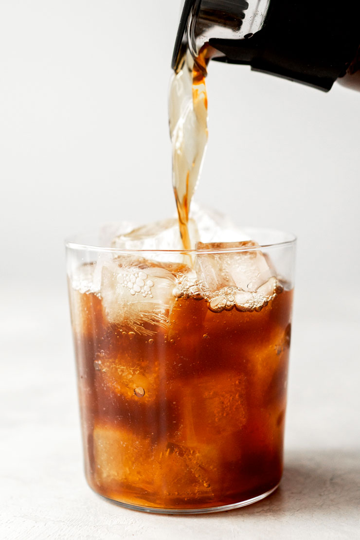 Pouring cold brew coffee into a glass filled with ice.