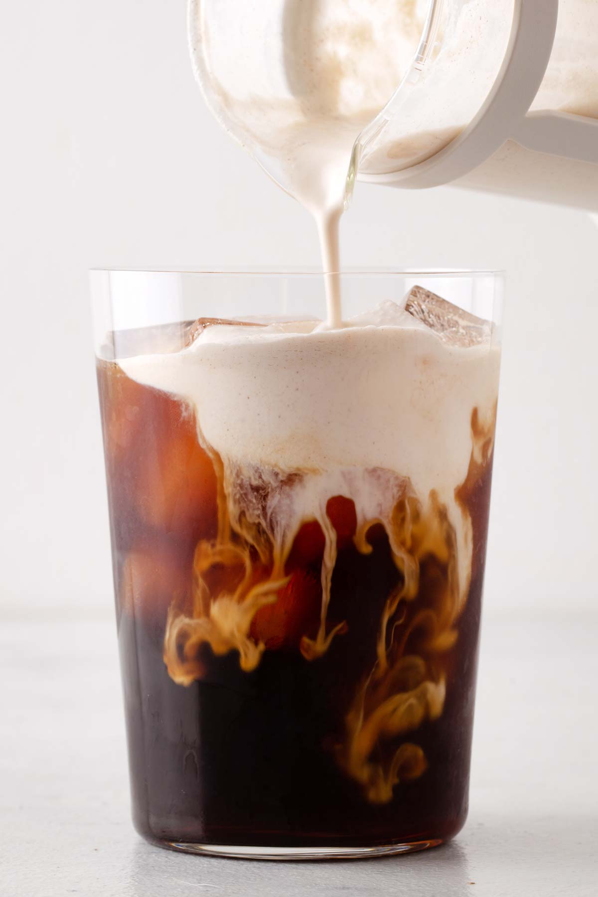 Brown Sugar Cold Foam being poured into a tall glass of iced coffee.