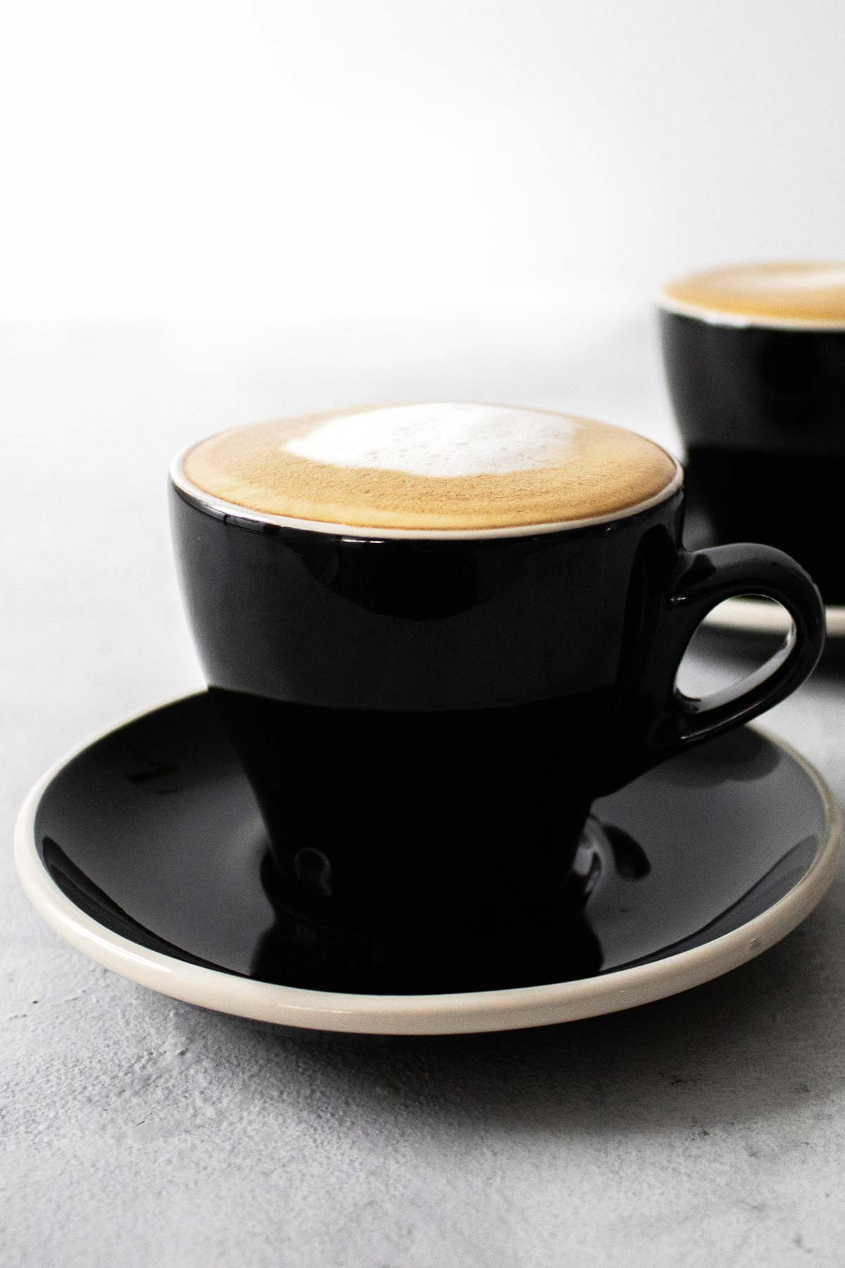 Two black cups with saucer filled with cappuccino.