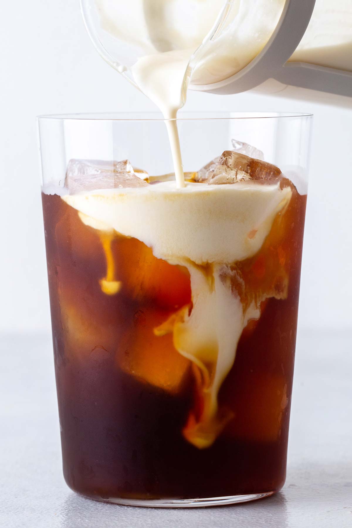 Carmel cold foam being poured into an iced coffee in a glass.