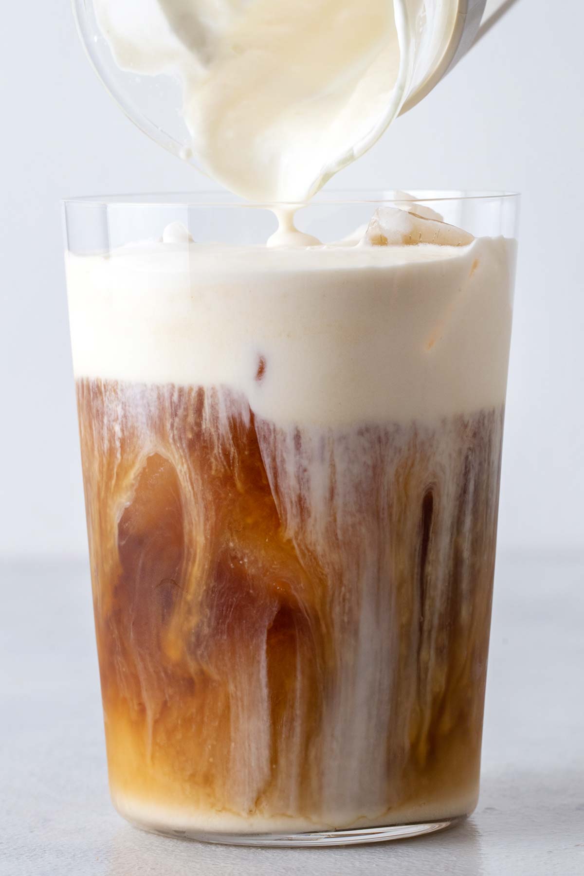 Caramel cold foam poured over an iced coffee in a glass. 