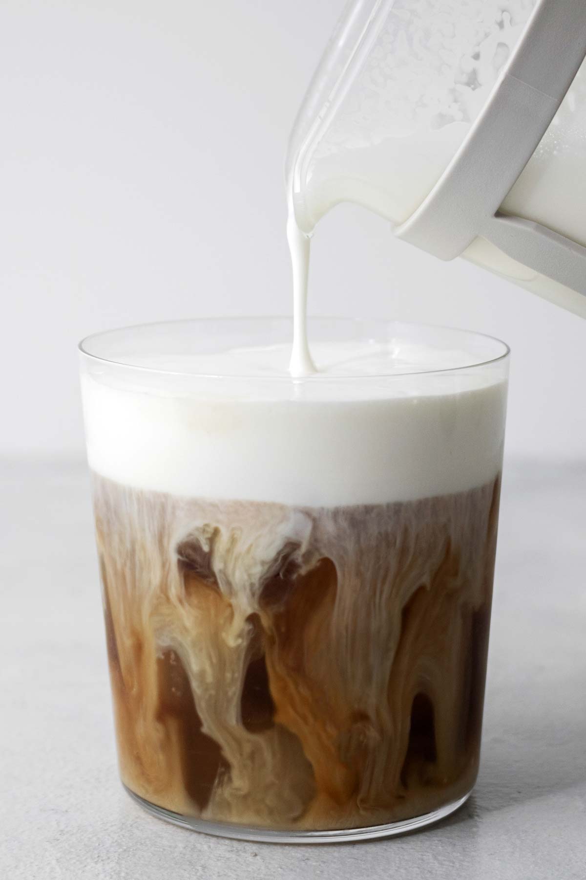 Pouring cold foam into a cup of iced coffee.