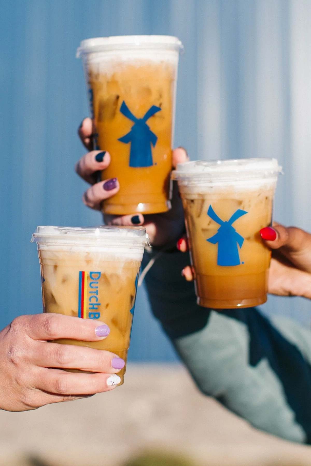 Three Dutch Bros iced drinks held up in the air.