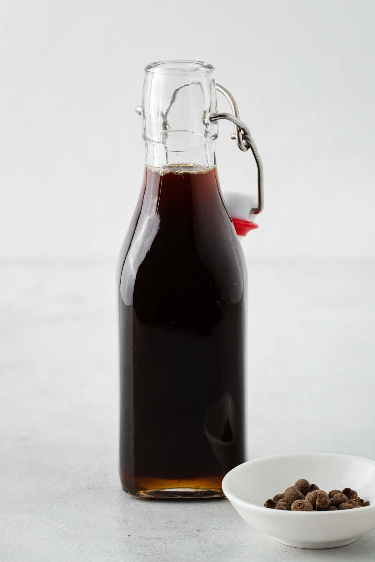 Gingerbread Syrup in a bottle next to a small bowl of allspice berries.