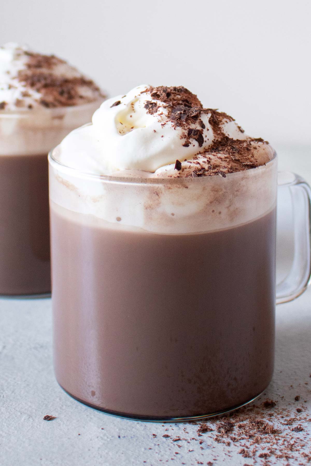 Two hot chocolates in glass mugs with whipped cream and grated chocolate.