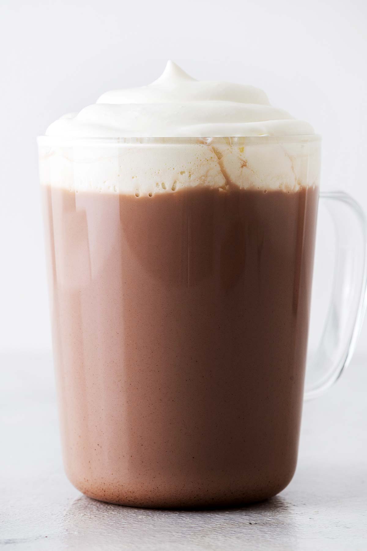 Homemade hot chocolate with whipped cream in a glass mug.