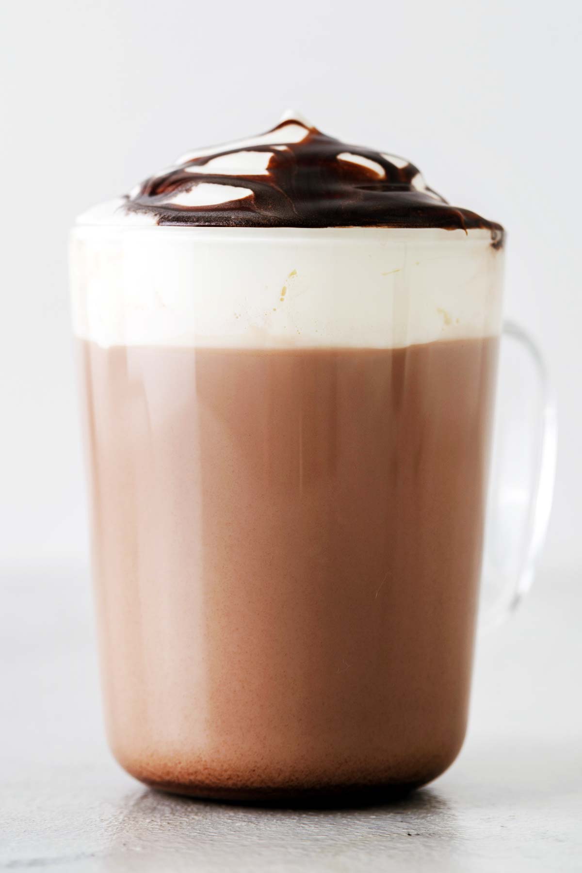 Homemade hot chocolate with whipped cream in a glass mug.