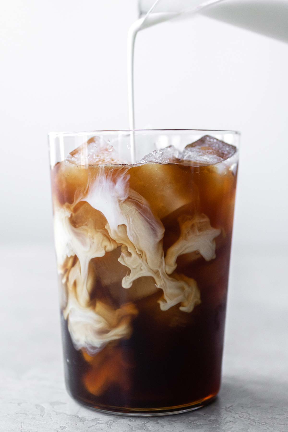 Pouring half & half into a cup of iced coffee.