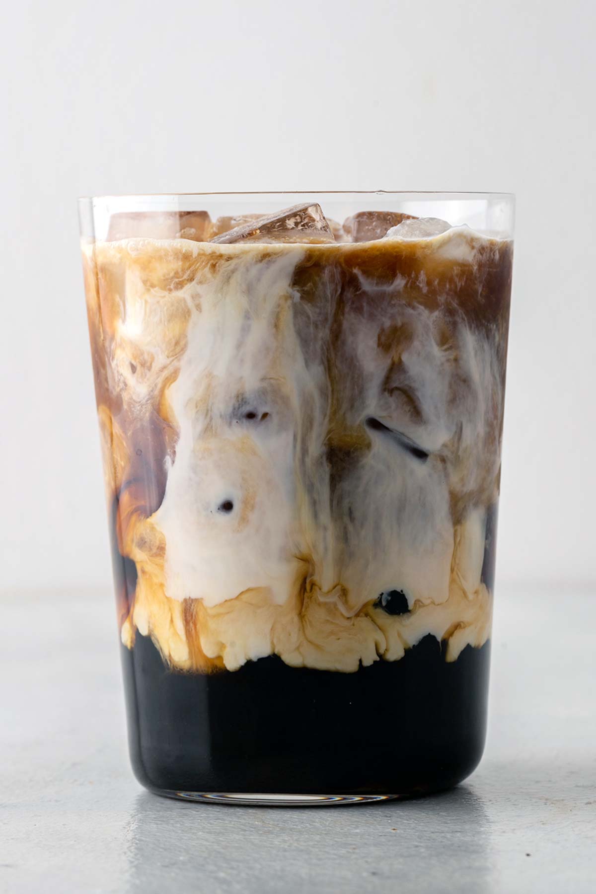 Es Kopi Boba dengan susu berputar dan boba di bagian bawah gelas bening.