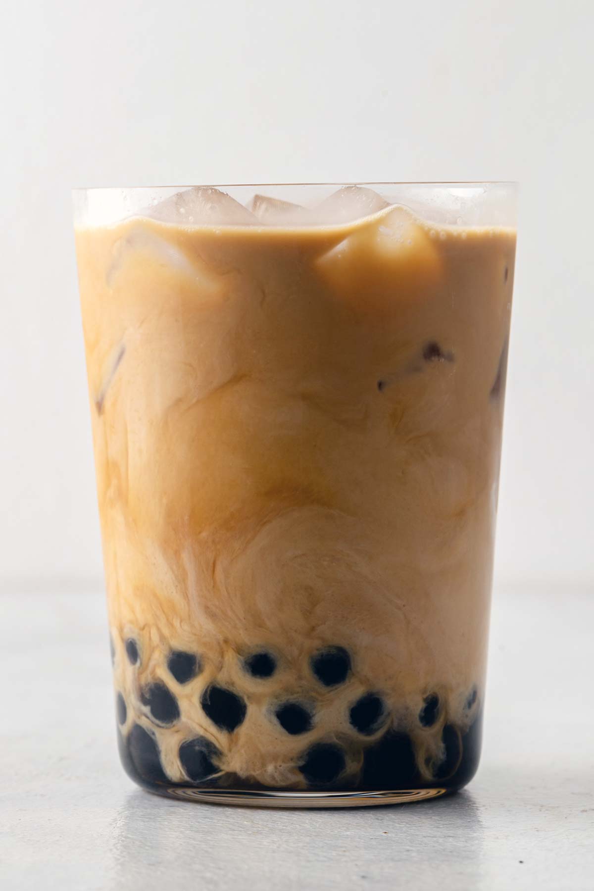 Iced Coffee Boba with the milk swirling in the glass and the boba at the bottom.