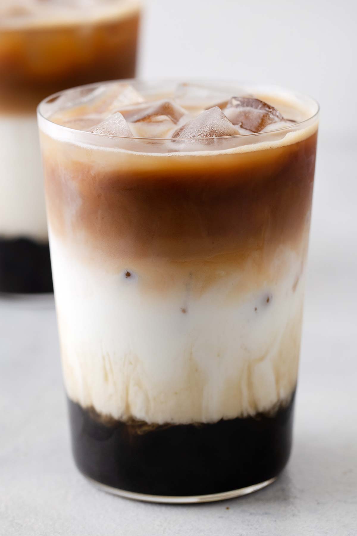 A layered iced latte with boba in a glass, served with an extra-wide straw.