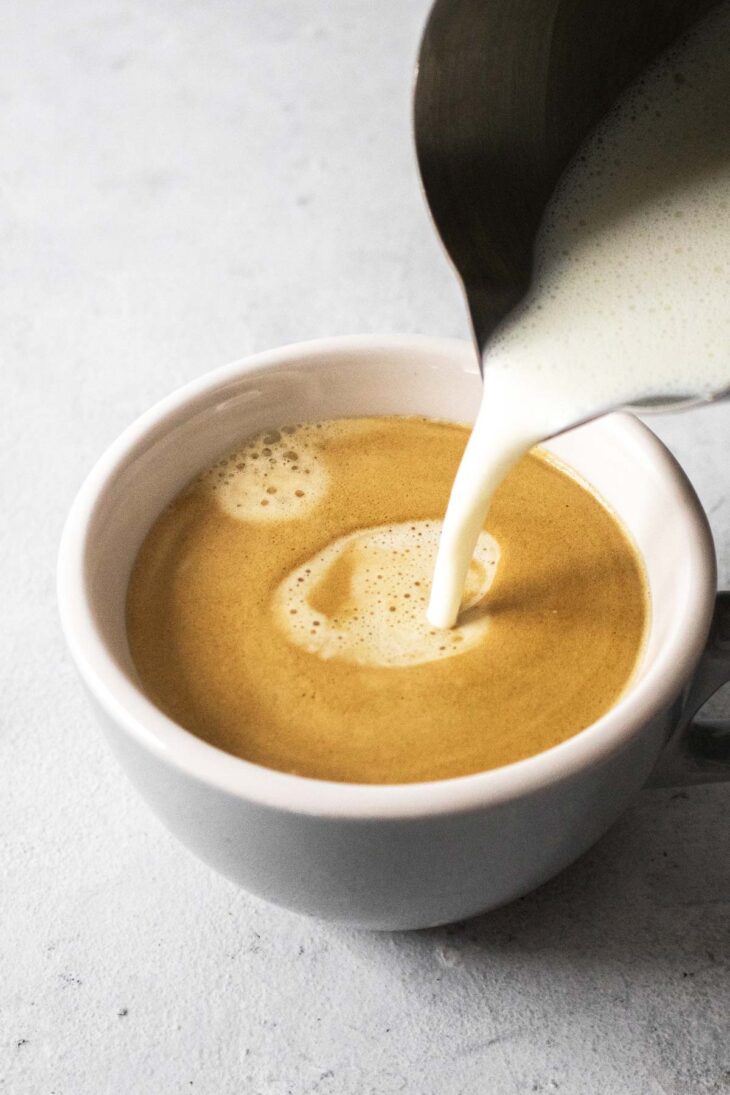 Pouring steamed milk into a mug with espresso.