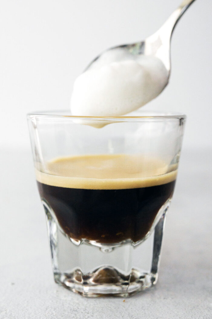 Spooning milk foam on top of espresso.