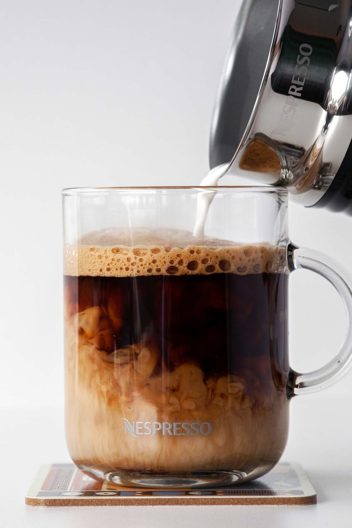 Pouring frothed milk into a Nespresso cup filled with coffee.