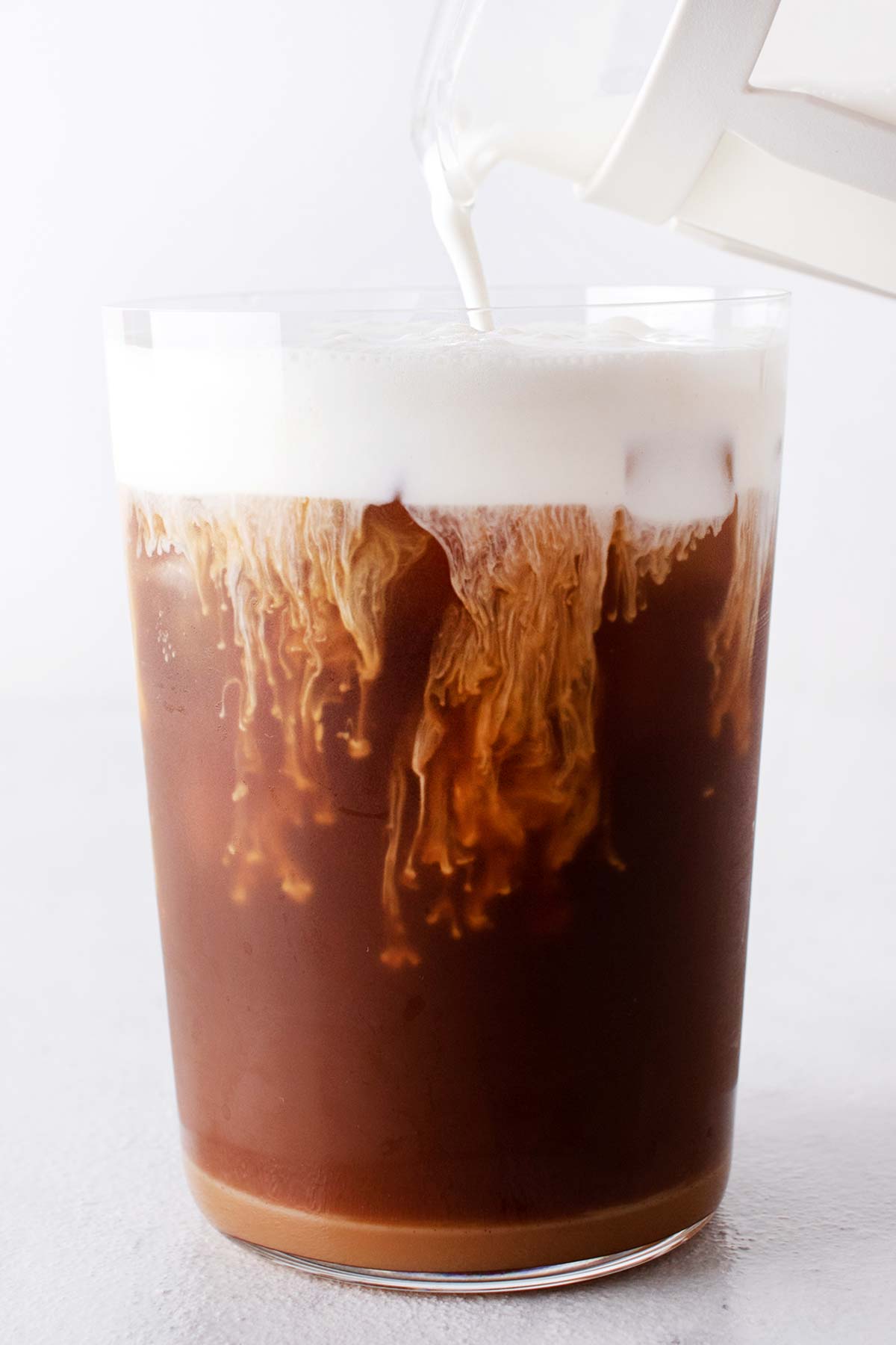 Pouring salted caramel cold foam on top of an iced coffee.