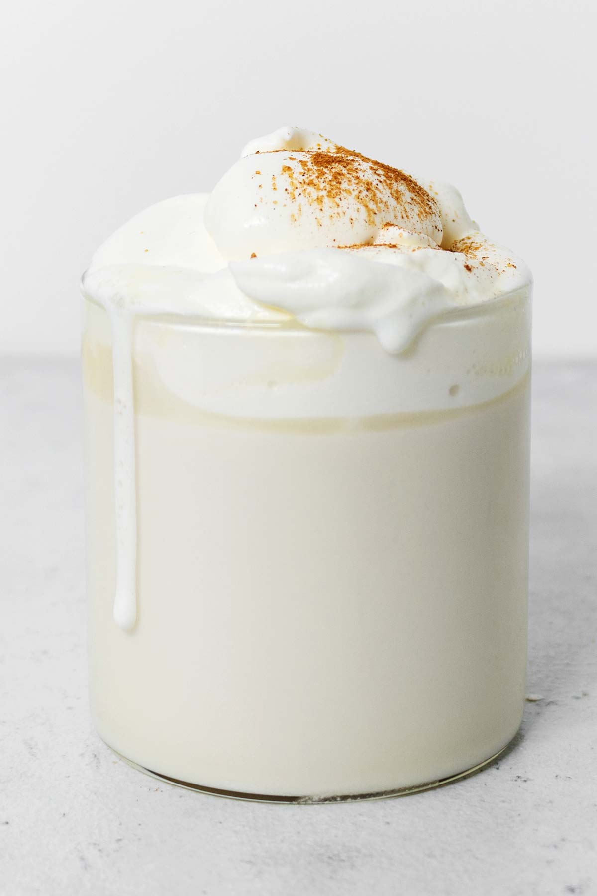 Snickerdoodle white hot chocolate drink with whipped cream in a glass mug.