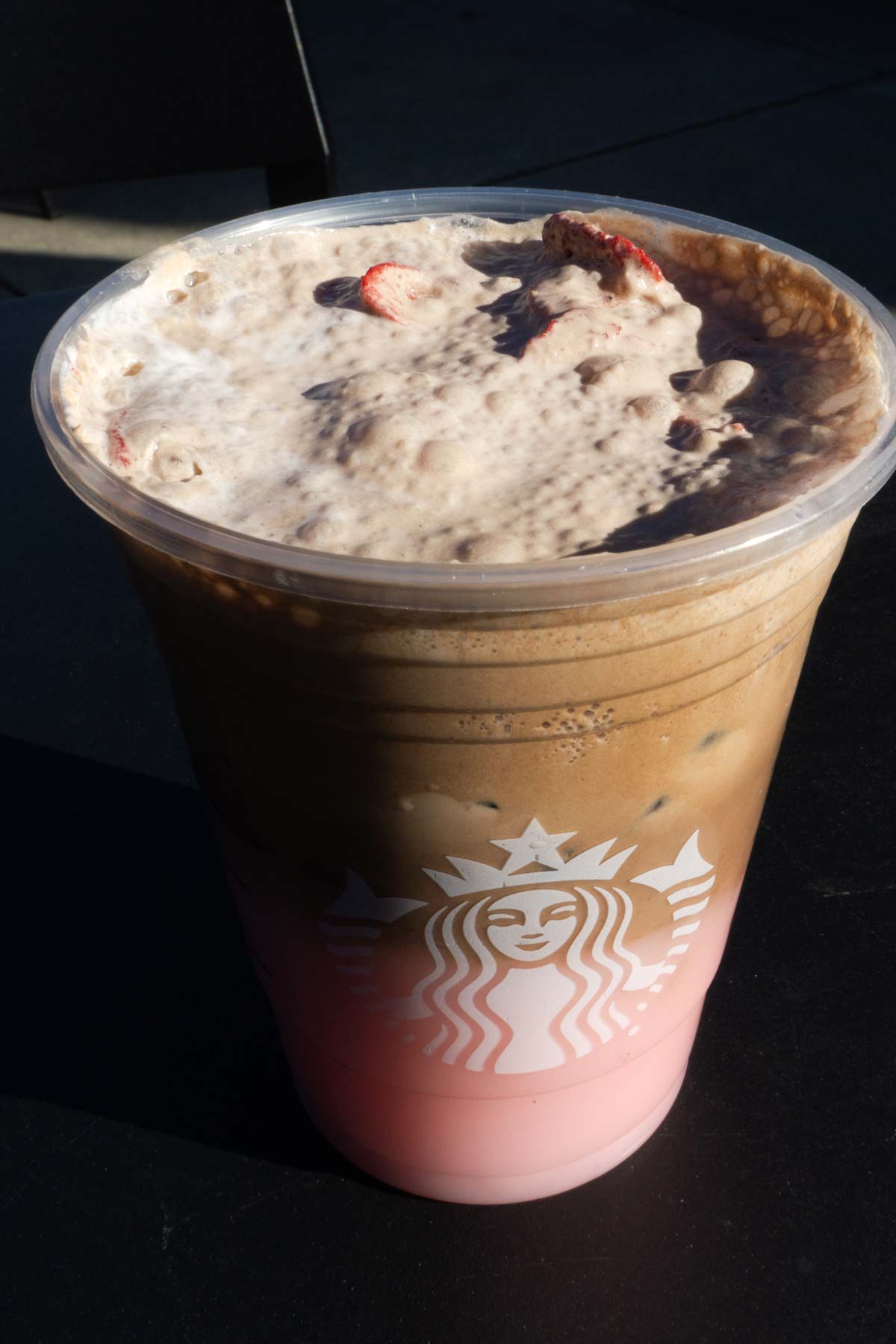 Large cup of Starbucks layered Pink Drink with chocolate cold foam in a cup with ice topped with dried strawberries.