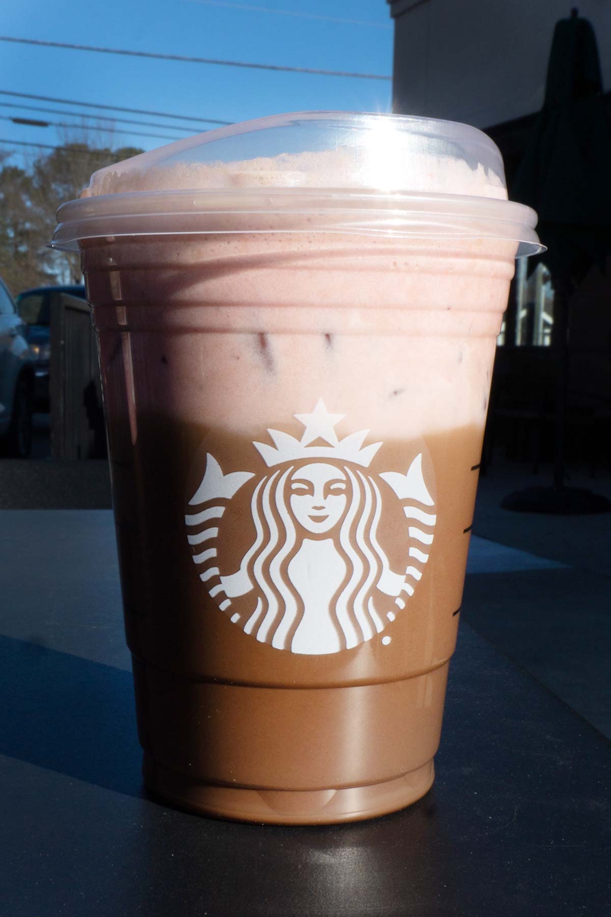 Grande sized Starbucks layered mocha and strawberry drink in a cup with a lid.