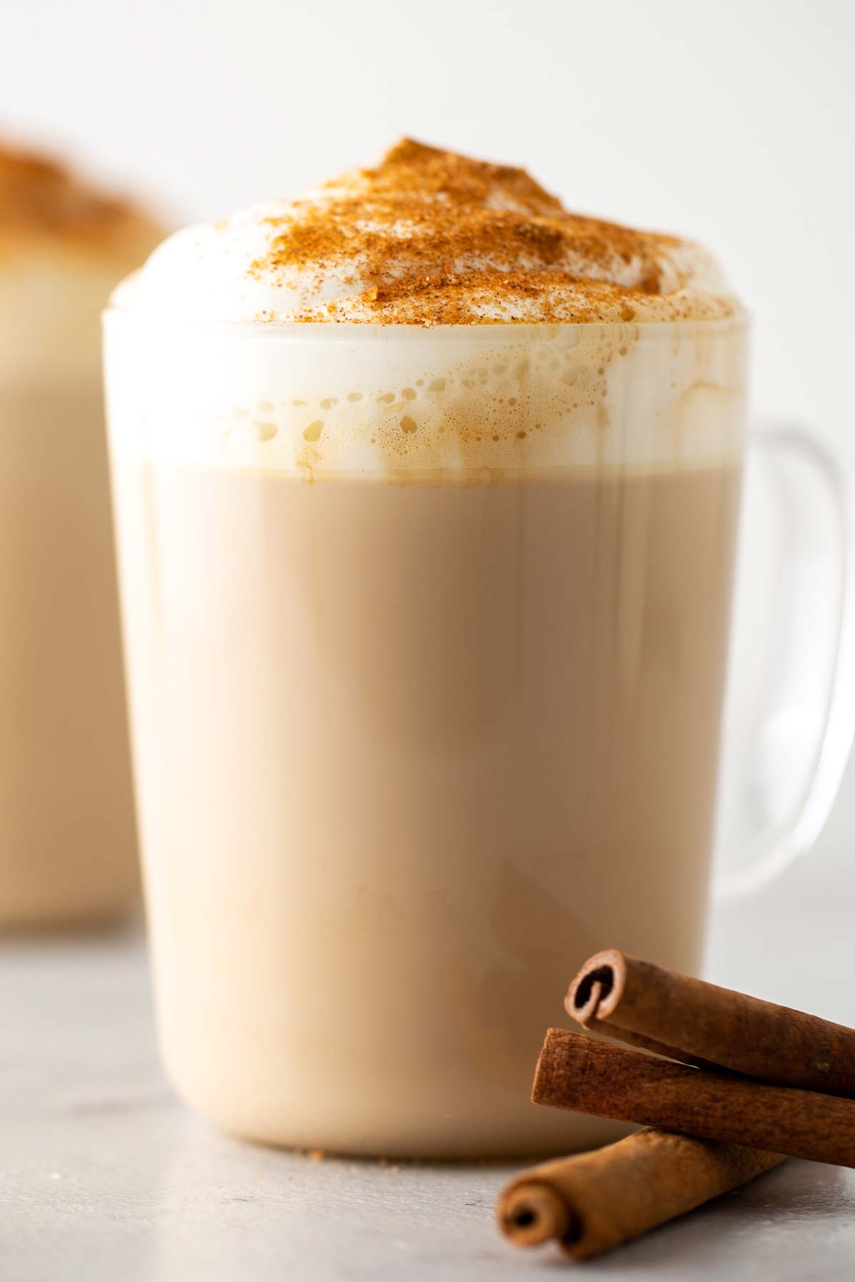 Minuman kopi Starbucks Cinnamon Dolce Latte dalam gelas mug dengan whipped cream dan topping kayu manis.