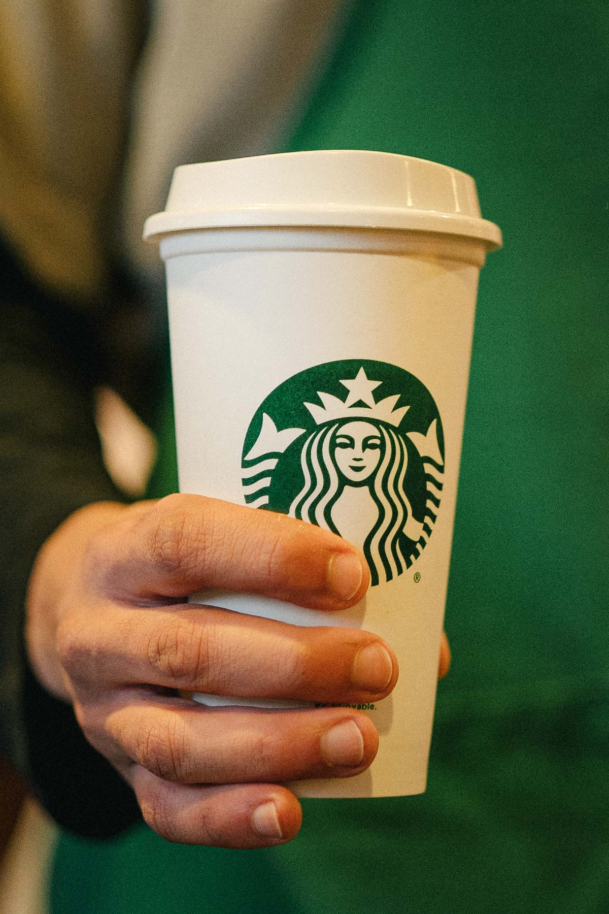Hand holding Starbucks cup with lid.