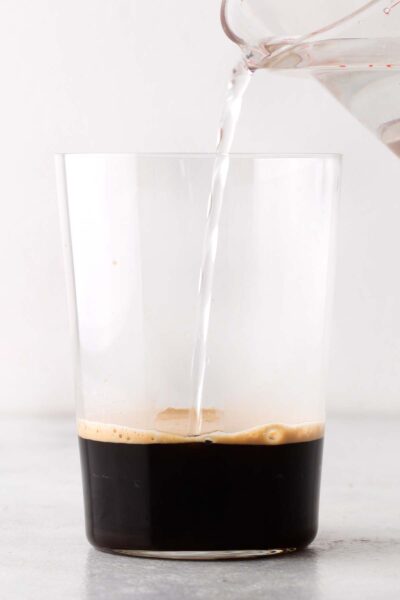 Pouring cold water into a cup with espresso.