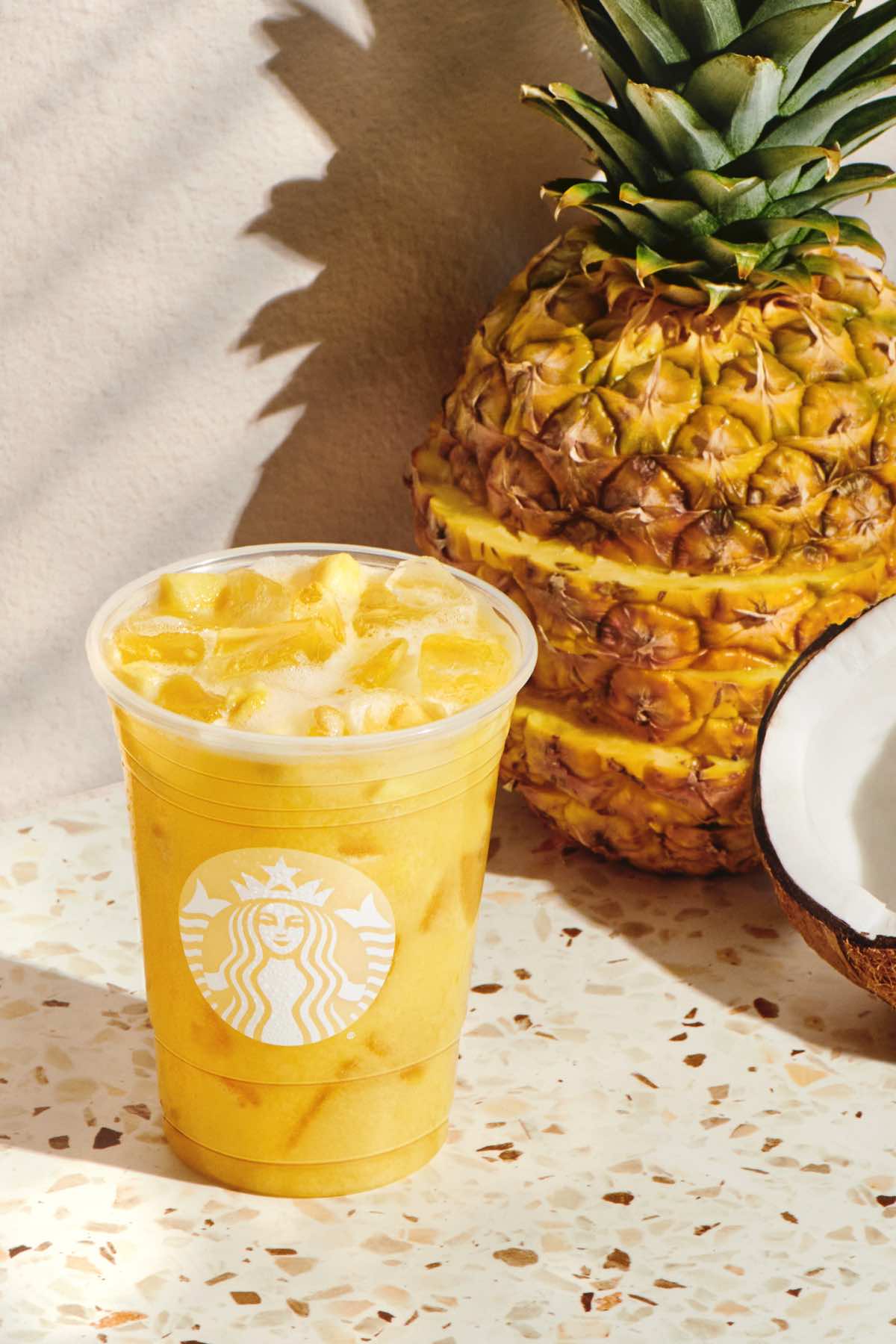 Paradise Drink in a Starbucks cup with pineapple and coconut behind the glass.