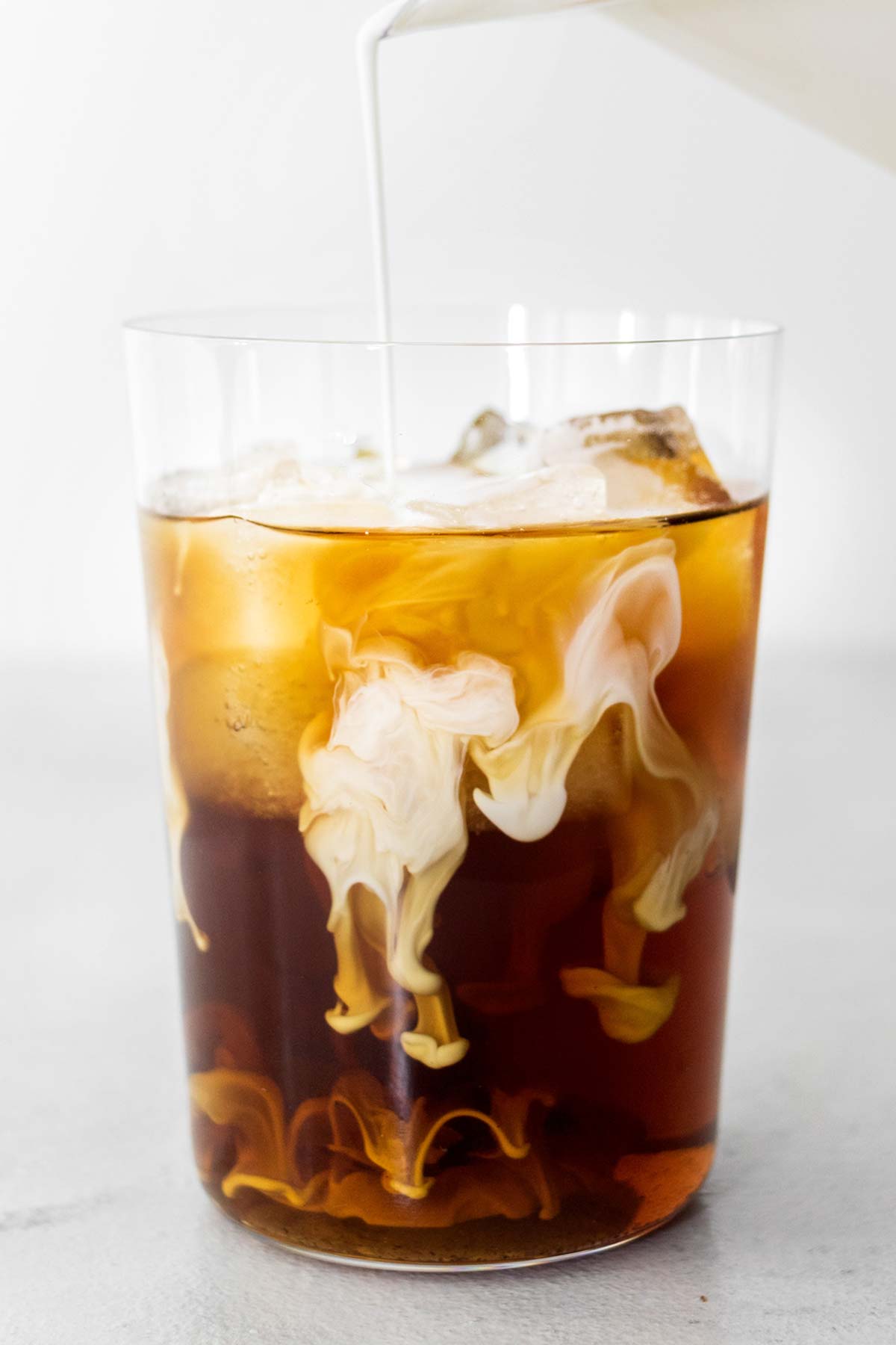 Pouring Sweet Cream into a cup of cold brew coffee with ice.