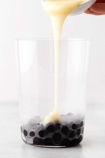Pouring condensed milk into a glass on top of tapioca pearls.